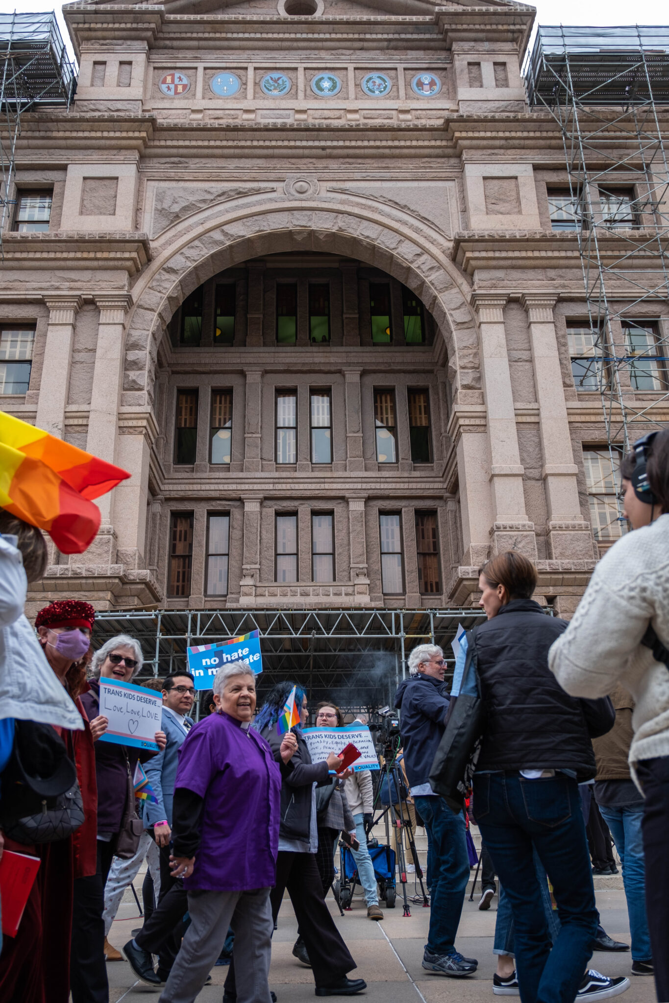 A crowd of people holding signs and pride flags gathered outside the Texas Capitol.