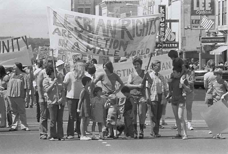 A black and white photo from 1976 of a group of people holding signs and banners marching on the street.