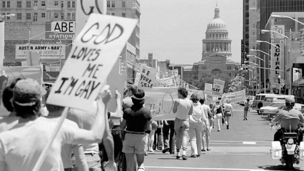 A black and white photo of people holding signs and marching down Congress Avenue toward the the Texas Capitol in the background.