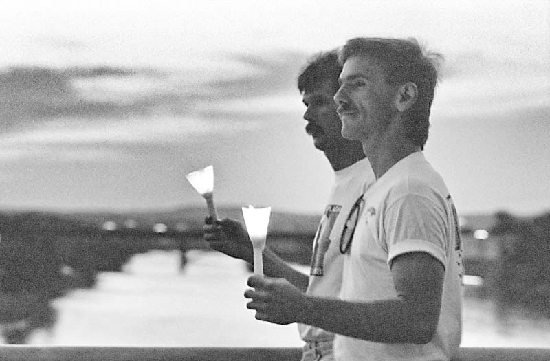 A black and white photo from 1989 of 2 men holding vigil candles.