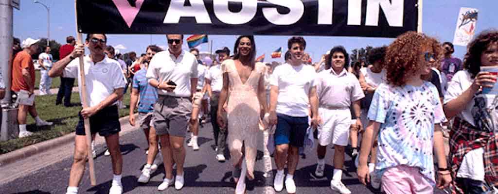 A color photo from 2002 of a crowd of people marching down the street at the Austin Pride Parade.