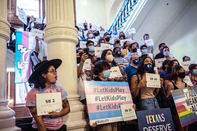 A color photo from 2021 of a crowd of people wearing masks and holding posters standing on the steps inside the Texas Capitol.