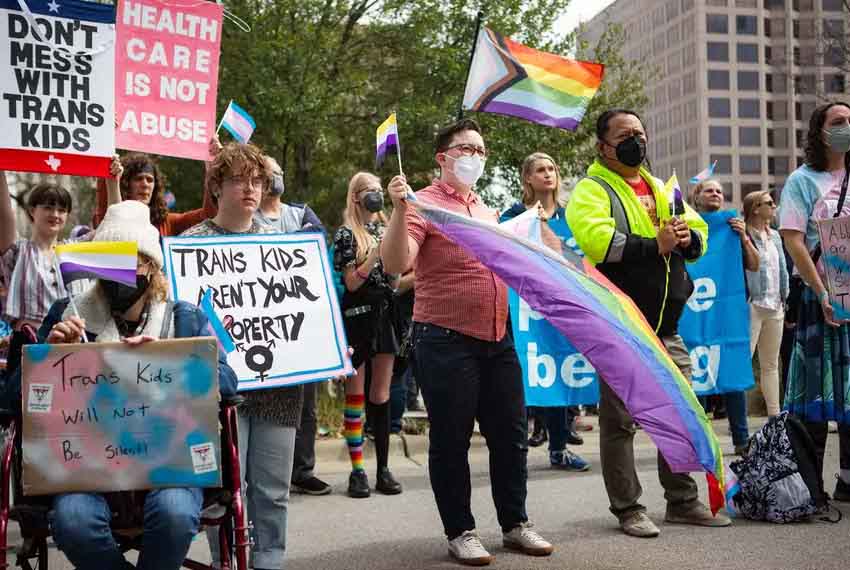 A color photo from 2022 of a crowd of people gathered outside the Texas Capitol holding banners, posters, and pride flags.