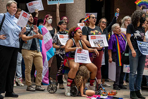 A color photo from 2023 of a crowd of people gathered in the outdoor rotunda of the Texas Capitol holding signs and chanting together.