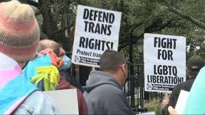 A color photo from 2024 of people holding up signs that read "Defend trans rights" and "Fight for LGBTQ liberation"